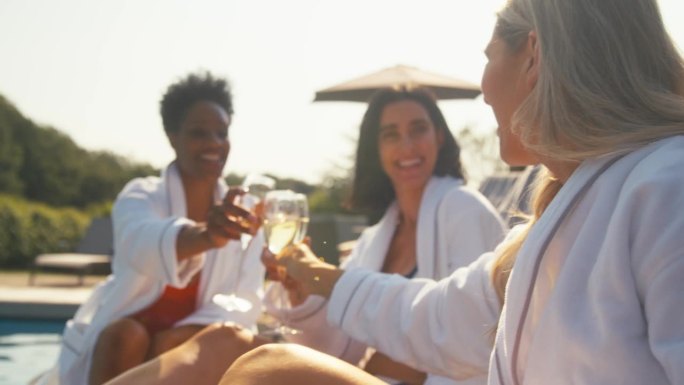 一群成熟的女性朋友在户外穿着长袍，躺在躺椅上喝着香槟