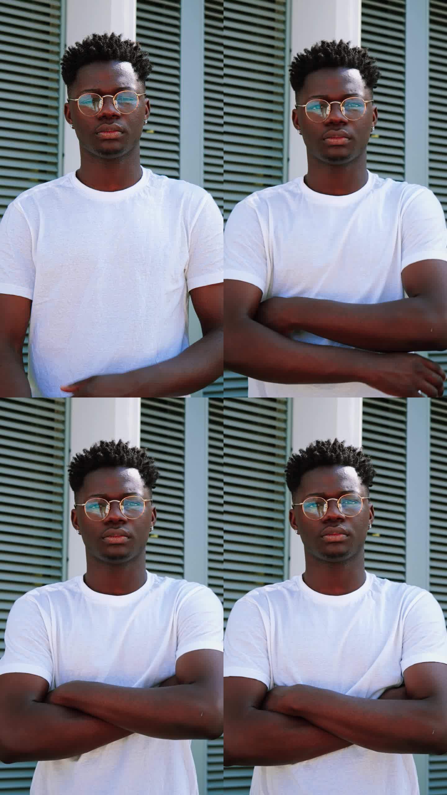 年轻的非洲裔美国人的垂直肖像严肃自信的家伙看着相机，双臂交叉站在外面。帅气的男学生在校园里摆出一副沉