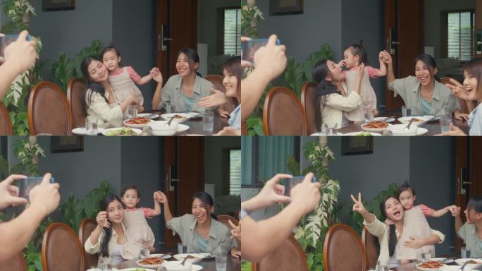 年轻的亚洲家庭用手机拍照，坐在后院的餐桌上玩得很开心。多代同堂的家庭一起享受消费。