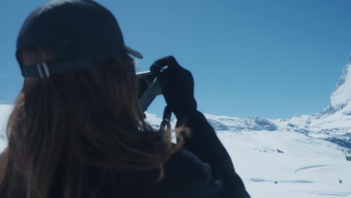 一个快乐的年轻女子在瑞士雪山度假的空闲时间拍照的后视图。