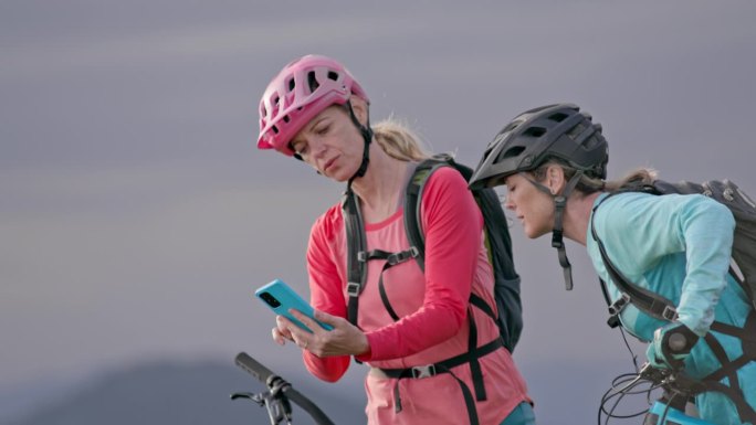 两个女山地自行车手看着智能手机，指着附近的小路