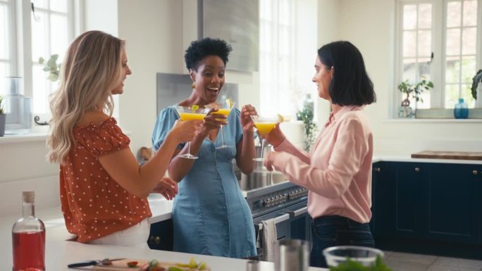 三个成熟的女性朋友在家里一起在厨房用鸡尾酒敬酒