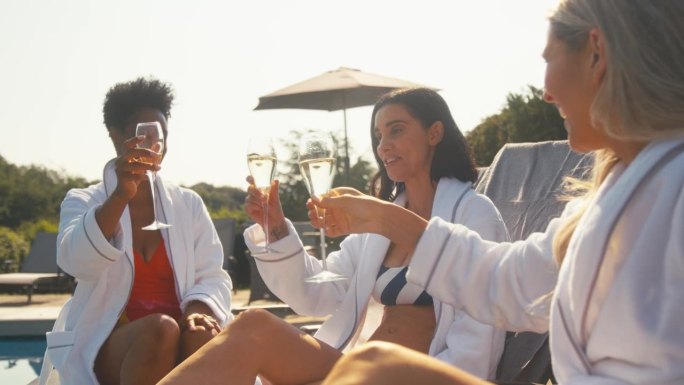 一群成熟的女性朋友在户外穿着长袍，躺在躺椅上喝着香槟