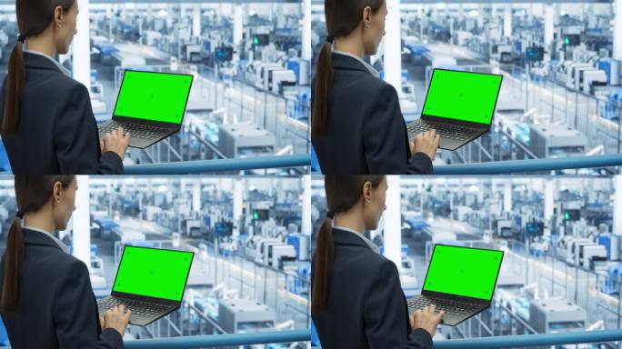 年轻的女工程师在电子厂使用绿屏模拟显示的笔记本电脑。越过肩膀的镜头。自动化制造机器和人工智能机器人被