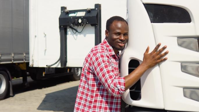 黑人卡车司机抱着他的卡车准备运输。快乐的非洲卡车司机热爱他的工作