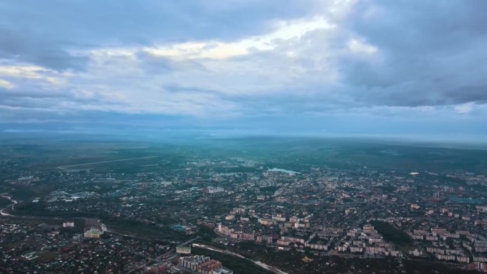 暴雨前，远处城市被雨云覆盖的高空鸟瞰图。多云天气下的飞机视角景观