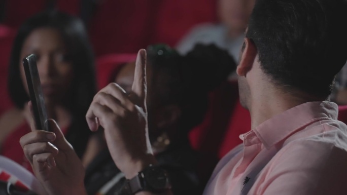 年轻的拉美裔男子在电影院看电影时用智能手机打电话，打扰了观众。电影放映期间禁止打电话。一个男人在剧院