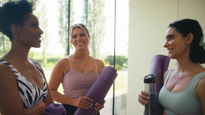 三个穿着健身服的成熟女性朋友在健身房或瑜伽课上拿着运动垫