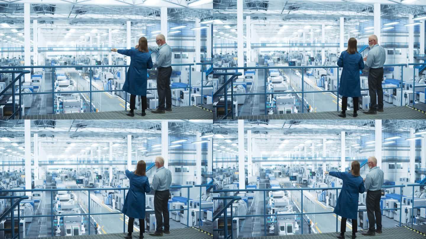 在一家现代人工智能自动化电子制造工厂，经验丰富的男女工程师站在平台上，背对着相机，使用笔记本电脑，讨