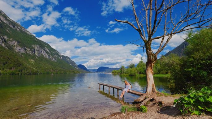 一名女子坐在美丽的Bohinj湖的木板路上摆动双脚