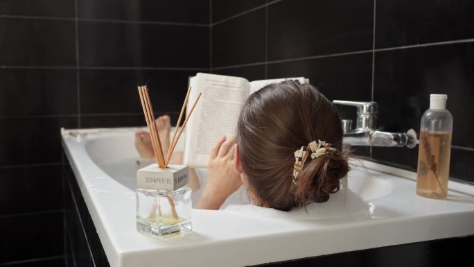 一个女人一边看书一边放松地洗澡。个人充实和心理健康的重要性