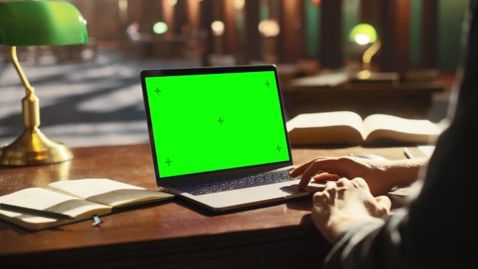 大学生使用绿屏模拟色度键显示笔记本电脑在经典图书馆学习。匿名者在线学习，浏览互联网，准备考试