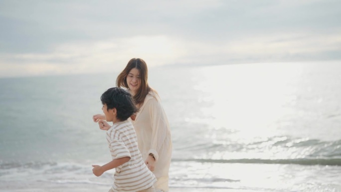 周末，快乐的亚洲母亲和孩子在海滩上愉快地放松。