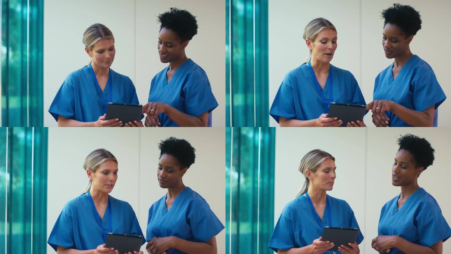 两个成熟的女医生穿着手术服拿着电子平板电脑在医院讨论病人的记录