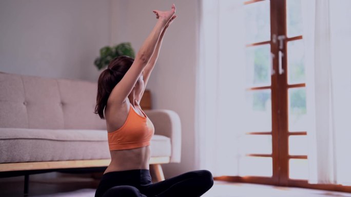 年轻漂亮，身材匀称，年轻运动的亚洲女士穿着运动服，在家里的健身垫上进行热身伸展运动。