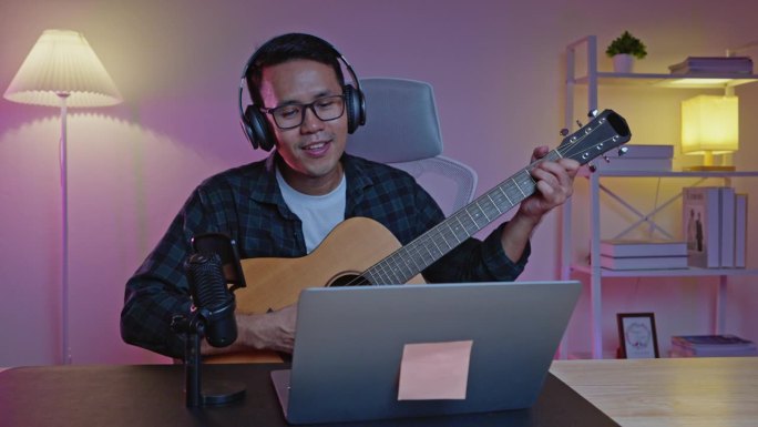 亚洲男子youtube直播表演弹吉他和唱一首歌。亚洲人在网上教吉他和唱歌。音乐家用笔记本电脑录制音乐