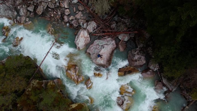 鸟瞰森林中的山河，一个人坐在水流中的巨石上