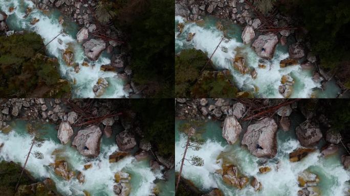 鸟瞰森林中的山河，一个人坐在水流中的巨石上