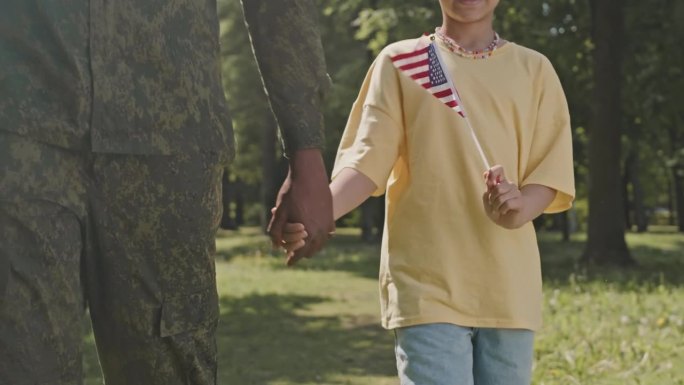 孩子手持美国国旗，与身穿军装的父亲同行
