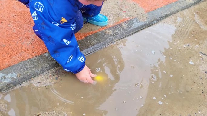 孩子在水坑里玩他的玩具玩得很开心，很享受手上的水和泥的感觉