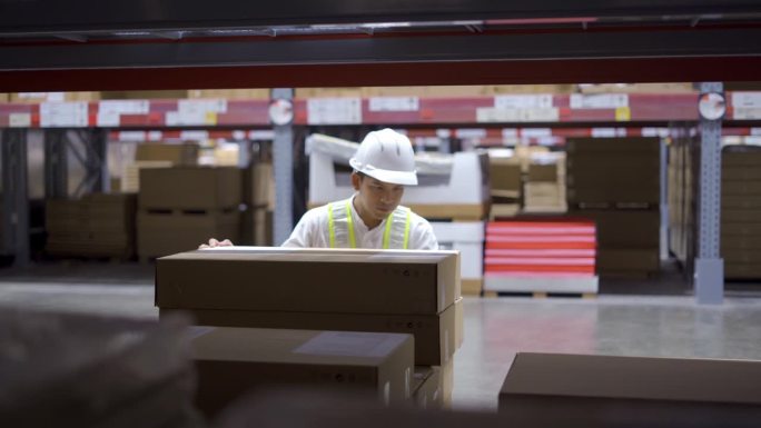 仓库工作人员戴安全帽，穿绿色反光安全服，在物流门店将箱子从货架上拿出来。