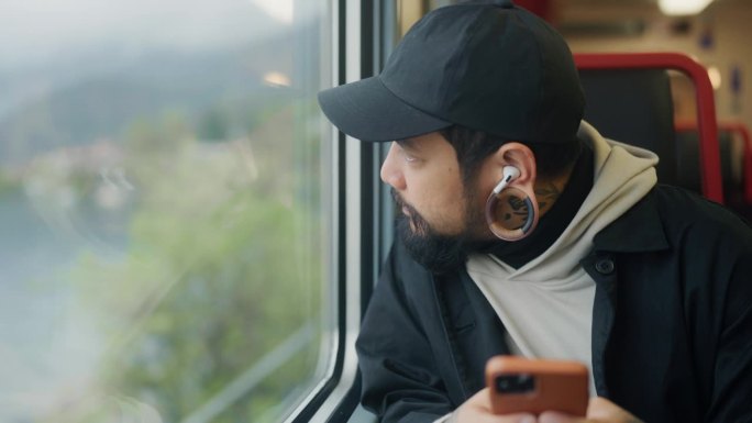 一名亚洲游客在火车上通勤，一边看手机，一边欣赏风景。