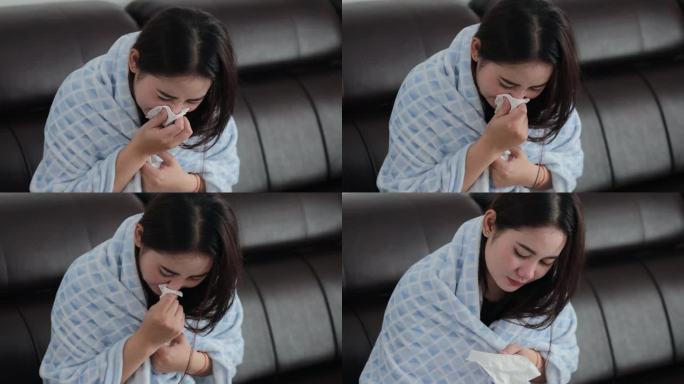 不健康的亚洲妇女裹着毯子吹感冒打喷嚏流鼻涕过敏流感咳嗽感冒打喷嚏。