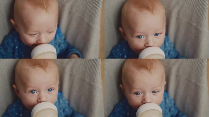 可爱的小男孩的高角度肖像享受奶瓶里的牛奶，同时放松在家里的保镖。蓝色的眼睛