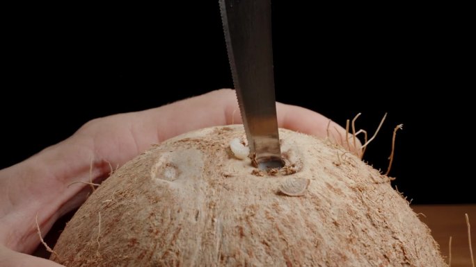 特写:一个男人手拿着椰子，在上面钻一个洞，插入一根稻草。