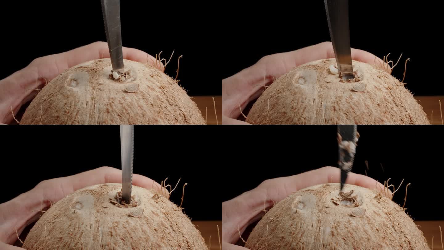 特写:一个男人手拿着椰子，在上面钻一个洞，插入一根稻草。