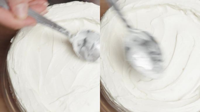 从上面看，一位糕点师正在把白色奶油涂在木桌上的蛋糕上。垂直视频。