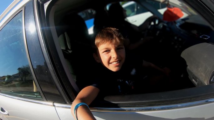 男孩坐在汽车的副驾驶座上，开心地看着开着的车窗