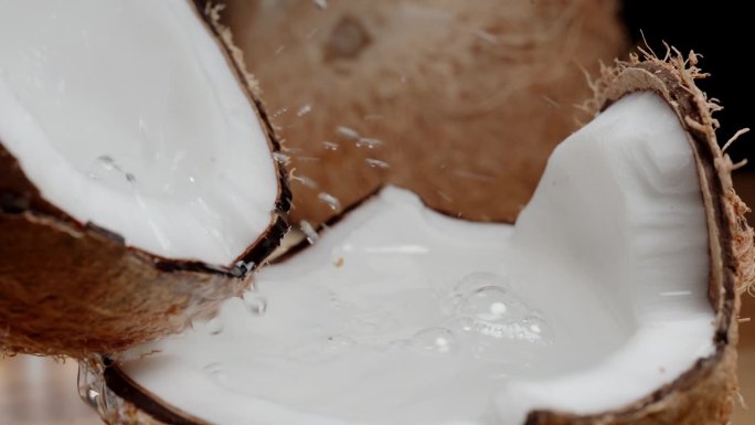 椰奶从断椰子的两半流出来，慢镜头。