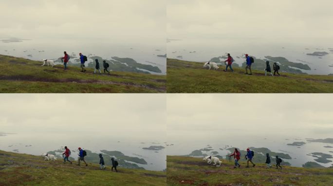 在一个下雨天，一个年轻的家庭带着两个孩子和一只白狗走上一座小山，俯瞰着北欧小镇的美景。无人机的观点。