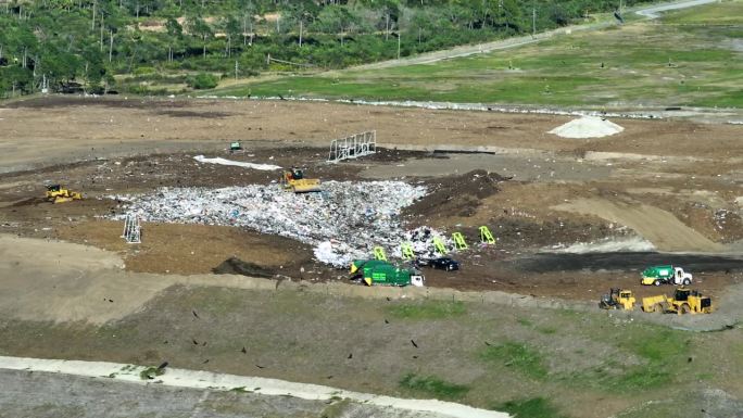 固体废物处理设施。堆填区垃圾场的垃圾管理。推土机拖拉机将大量垃圾埋在地下。现代消费主义对环境的有害影
