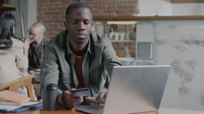 满意的非洲裔美国企业家使用笔记本电脑和信用卡在联合办公办公室进行交易