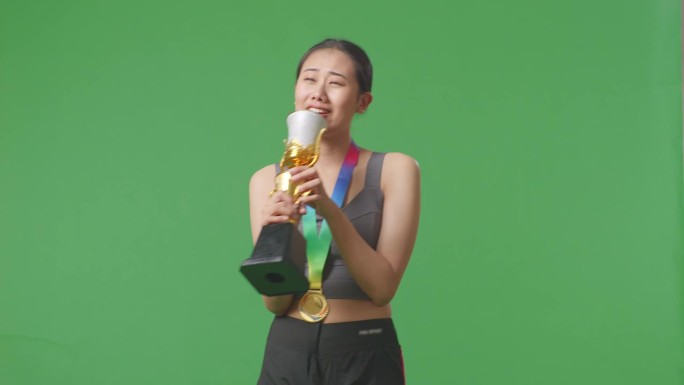 获得金牌的亚洲女子在金杯上唱歌庆祝自己成为首个冠军，绿幕背景在演播室