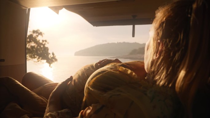 在阳光明媚的日子里，一名孕妇坐在面包车上看着美丽的湖泊，抚摸着自己的肚子