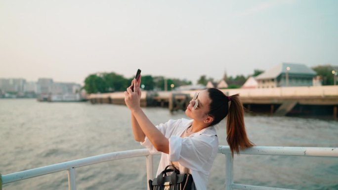 年轻的亚洲女子在泰国旅游时拍摄自己和美丽的河滨景色。