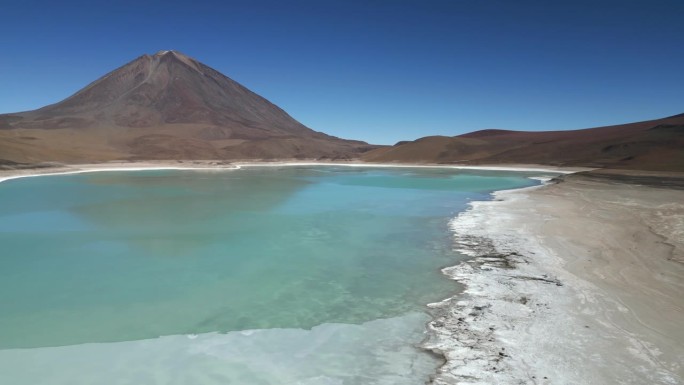在一个寒冷的冬日，空中无人机从右到左拍摄了玻利维亚一座山脚下一个部分结冰的大湖。