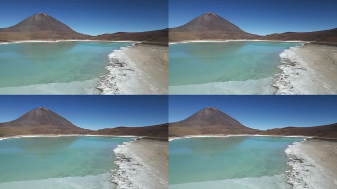 在一个寒冷的冬日，空中无人机从右到左拍摄了玻利维亚一座山脚下一个部分结冰的大湖。