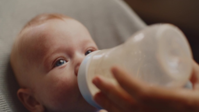 小男孩在家里用妈妈喂的奶瓶喝牛奶的特写