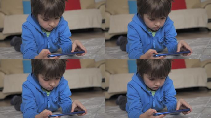 孩子躺在地板上玩手机。孩子在手机上玩电子游戏。男孩玩电子游戏智能手机。孩子用手机玩游戏、在线教育和社