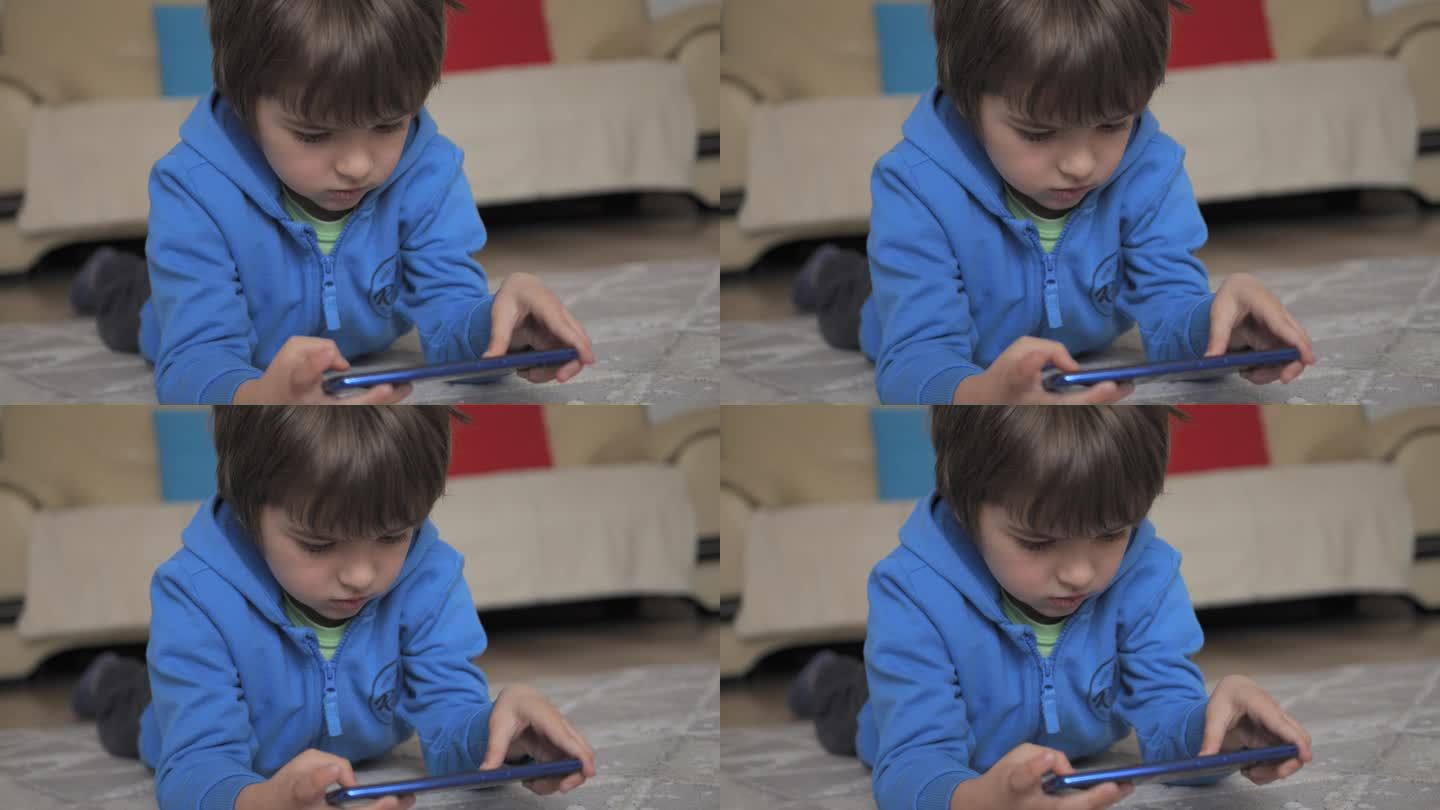 孩子躺在地板上玩手机。孩子在手机上玩电子游戏。男孩玩电子游戏智能手机。孩子用手机玩游戏、在线教育和社