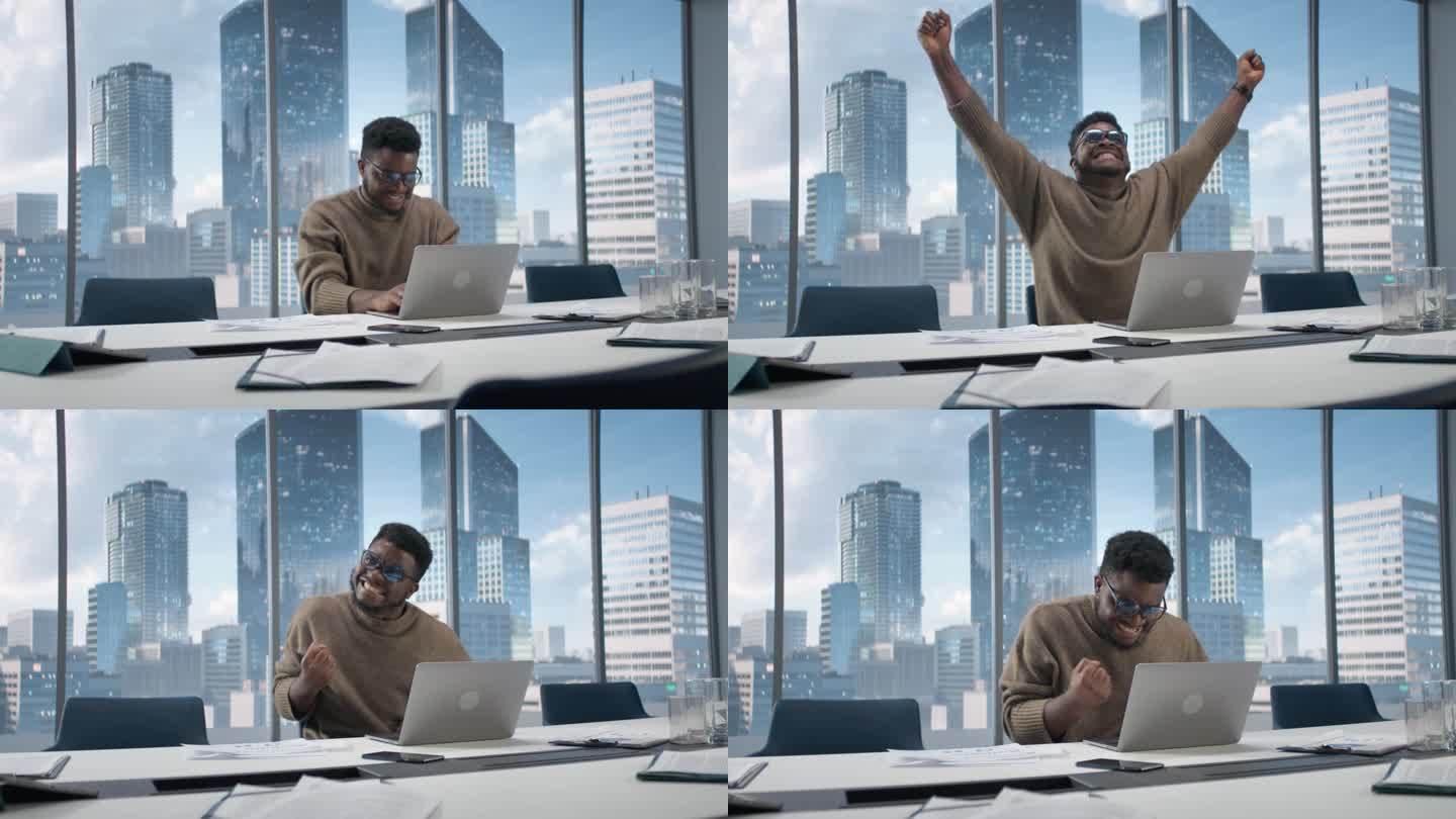 黑人商人坐在摩天大楼办公室的办公桌前，用笔记本电脑工作，情绪激动地庆祝电子商务交易的成功。非裔美国企