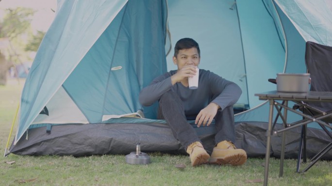 一个亚洲人坐在露营帐篷里，在国家公园里喝着茶。