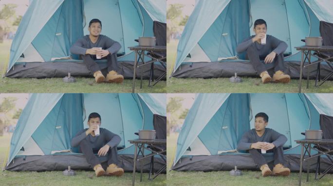 一个亚洲人坐在露营帐篷里，在国家公园里喝着茶。