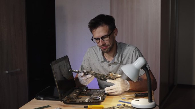 戴眼镜的修理工带着沮丧的神情检查着笔记本电脑的主板。