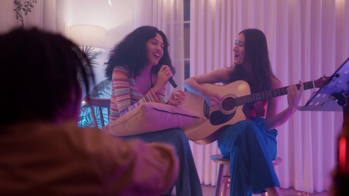 两个十几岁的女孩在家里的客厅里和多民族的朋友一起弹吉他，开心地唱歌。