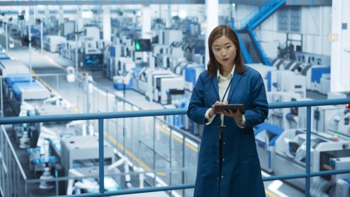 有思想的亚洲工程师在一个原始的现代电子工厂监测和分析条件，在人工智能软件的帮助下，自动机器人手正在工